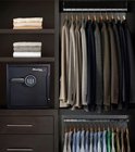 Zwarte Master Lock kluis met digitaal cijferslot in een inbouwkast naast kleding.