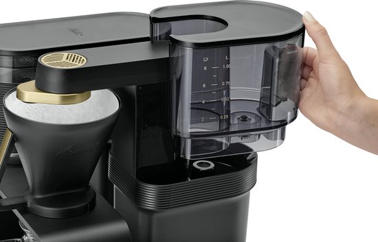Een hand vult een transparant waterreservoir met markeringen voor liter-aanduiding op een zwart koffiezetapparaat.