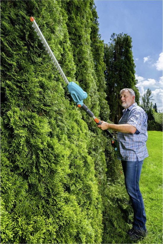 Man snoeit een hoge, groene heg met een turquoise heggenschaar met steel.