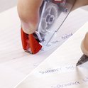 Montage de gros plans: une main utilise un rouleau correcteur Pritt mini sur une ligne écrite, et une main écrit avec un stylo sur un cahier.