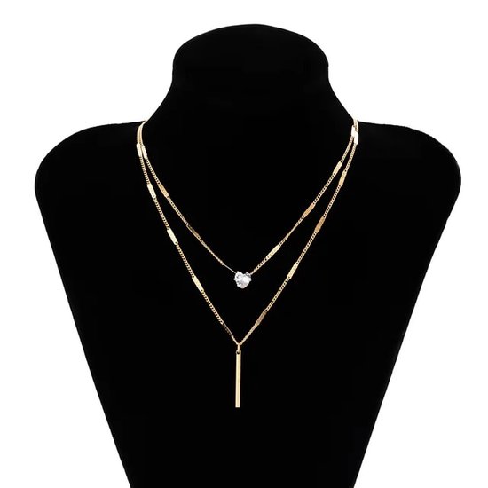 Gouden dubbele ketting met zirkonia hartje en staafje, op zwarte paspop.