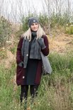 Model met donkerrode gebreide cardigan, jurk, sjaal en grijze handschoenen en muts.