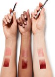 Drie armen met verschillende huidtinten waarop swatches van lipsticks zijn aangebracht, met de lipsticks vastgehouden in de handen.