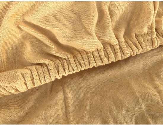 Detailopname van de ronde elastiek aan de rand van een okergeel jersey hoeslaken.