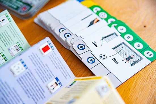 Kaartspel met afbeeldingen van voetbalacties en goals, deels op een houten tafel.