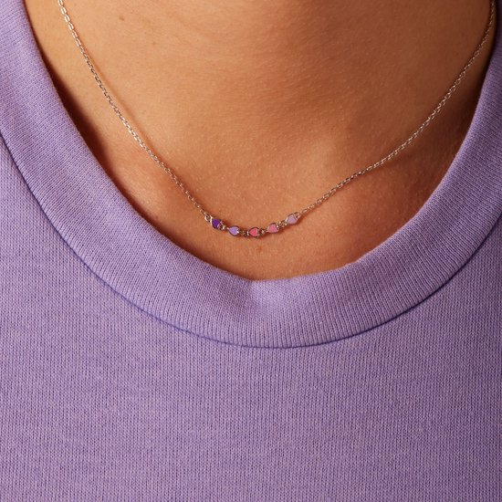 Zilverkleurige ketting met zeven gekleurde emaille hartjes (paars, roze) gedragen door een meisje met paarse trui.