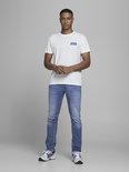 Man van voren gezien in een witte t-shirt met Jack & Jones logo en lichte spijkerbroek.