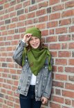 Een jong meisje met een groene gebreide muts en sjaal, en een grijze spijkerjas.