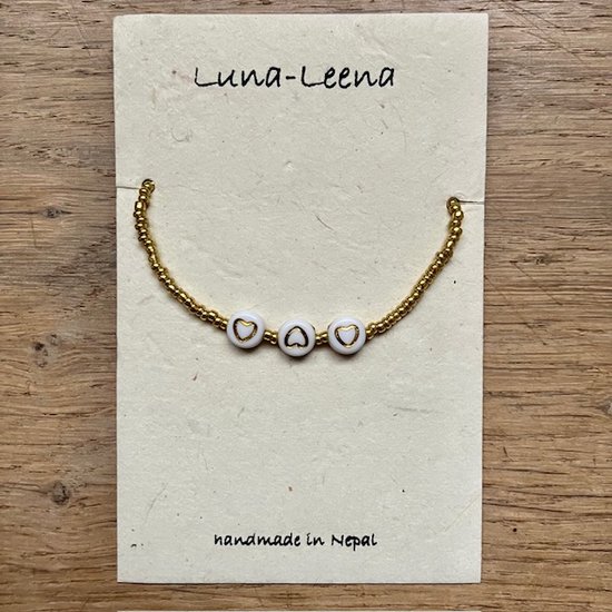 Gouden armbandje met witte kraaltjes en gouden hartjes op een kaartje met "Luna-Leena handmade in Nepal".