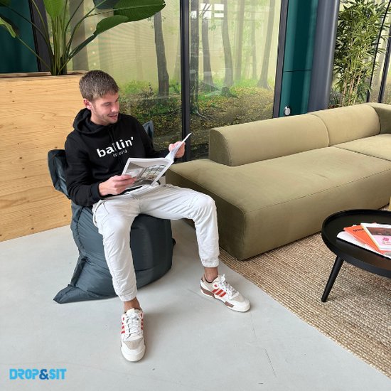 Man zit op een donkergrijze zitzak, leest een tijdschrift.