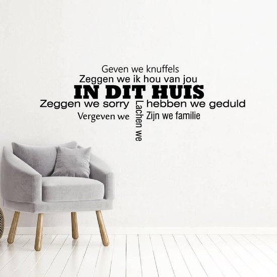 Zwarte muursticker met de tekst "IN DIT HUIS" en familie-waarden boven een grijze fauteuil.