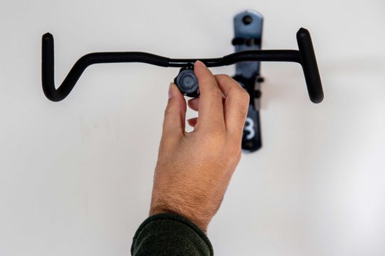 Hand verstelt zwarte fietsophanging aan de muur.