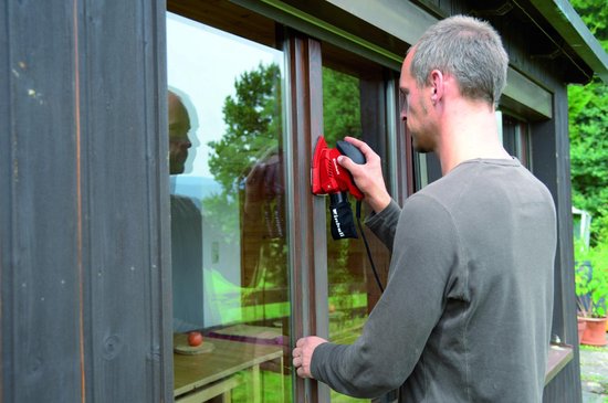 Man schuurt een houten kozijn met een rode Einhell schuurmachine met stofzak.
