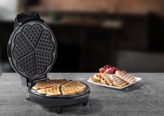 Open Bestron wafelijzer met vier hartvormige wafels erin. Naast het wafelijzer ligt een bord met wafels en fruit.