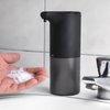 Zwarte automatische zeepdispenser die schuimzeep afgeeft in een hand bij een kraan.
