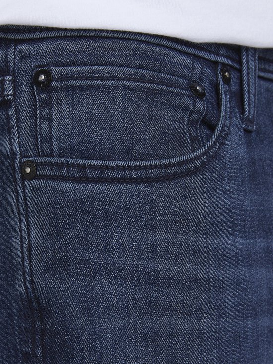 Detailopname van de blauwe spijkerbroek met een klein zakje, knopen en stiksels.