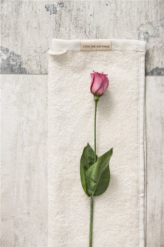 Crèmekleurige badhanddoek met 'LOVE THE SOFTNESS' label en roze bloem.