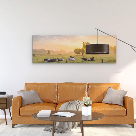 Panorama canvas met koeien in de wei bij zonsopgang, liggend op groen gras onder een warme, oranje lucht.