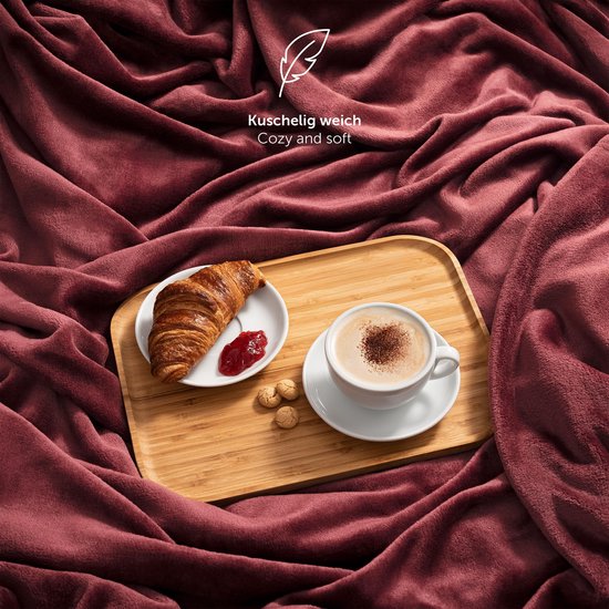 Bordeauxrode deken met een croissant, jam en koffie op een dienblad.