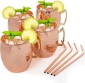 Vier koperen Moscow Mule bekers met rietjes, ijs, munt en limoen, op een witte achtergrond.