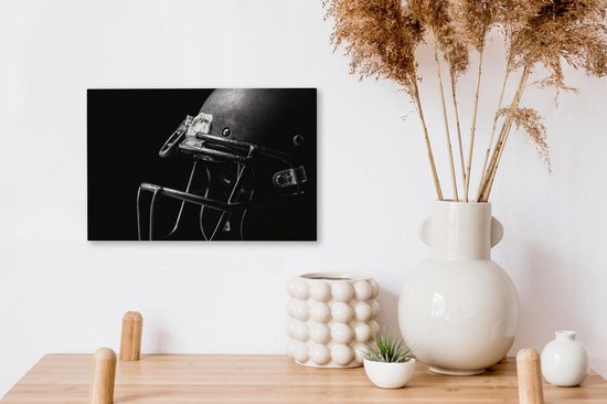 Un casque de football américain noir avec masque en acier, accroché à un mur blanc à côté d'un vase de fleurs séchées.