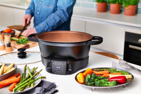 Zwarte multicooker met koperkleurige binnenkant, omringd door verse groenten.
