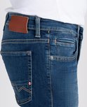 Detail van een donkerblauwe spijkerbroek met een bruin label en oranje stiksels.