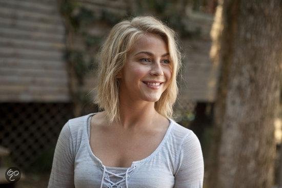 Een blonde vrouw met een grijze top met veterdetails, met kort, warrig haar en blauwe ogen.