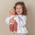Een meisje met krullend haar houdt een pop met roze outfit vast.