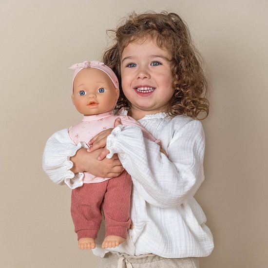 Een meisje met krullend haar houdt een pop met roze outfit vast.