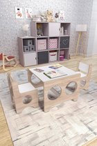 Kindertafel met 2 stoeltjes, wit blad en houten onderstel met ronde uitsparingen. In een kinderkamer met speelgoed.