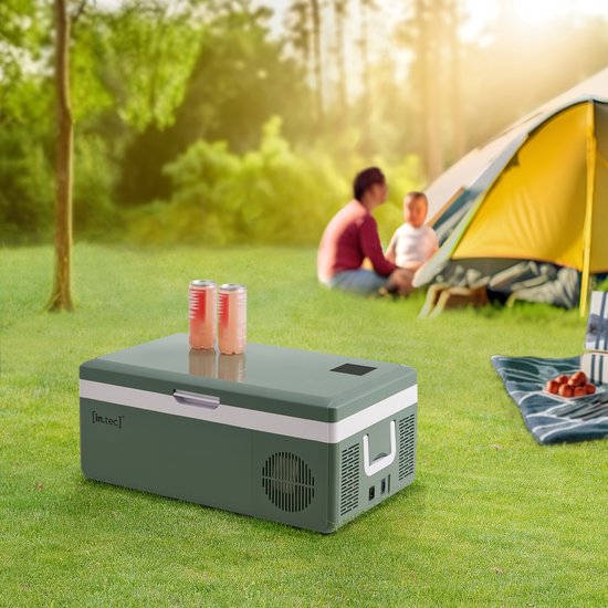 Legergroene koelbox met witte rand, staand in gras bij een tent met twee personen.