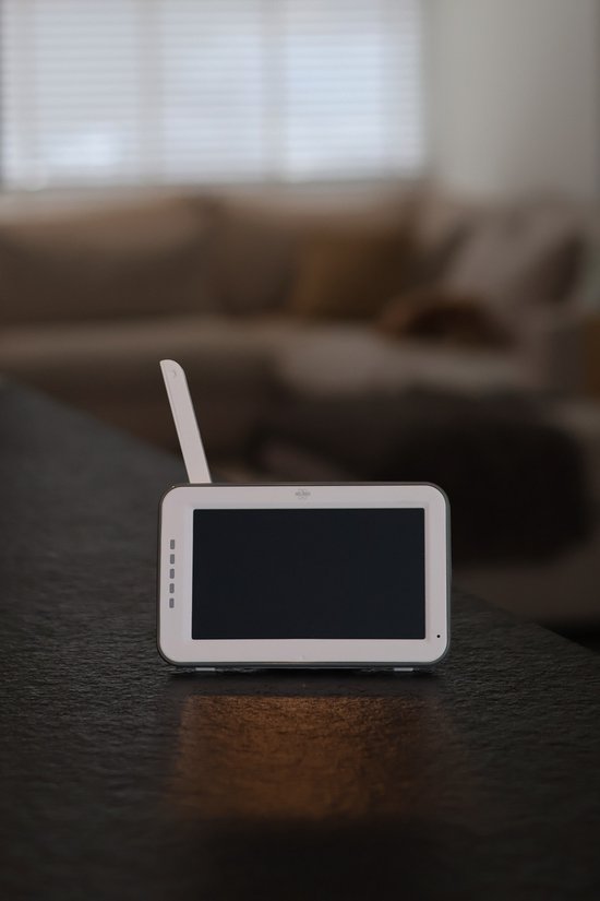Witte babyfoon monitor met antenne op een donkere tafel.