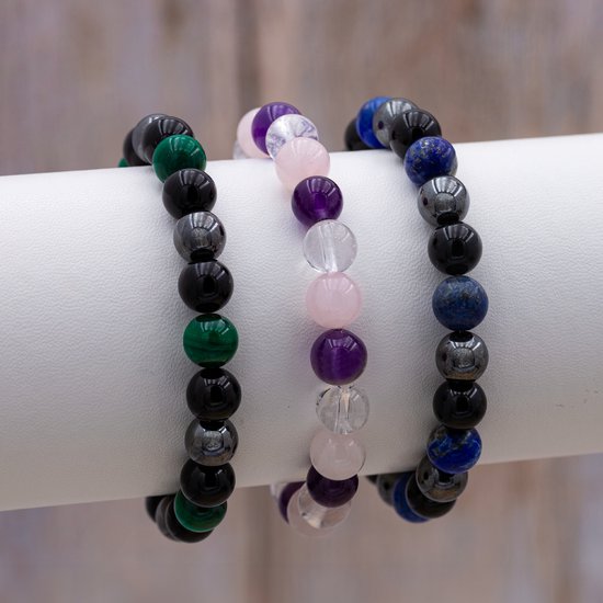 Drie armbanden op een witte standaard. De rechter armband bevat blauwe lapis lazuli, onyx en hematiet kralen.