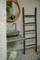 Donkergrijze houten decoratieve ladder met vijf sporten, staand naast een badkamermeubel met wasbak en ronde spiegel.