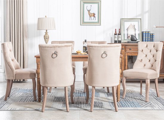 Achterkant van beige fluwelen eetkamerstoelen met hoge rugleuning en ringdetail.
