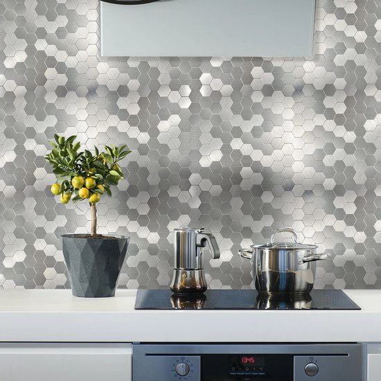 Zilverkleurige hexagon tegels met geborstelde afwerking, op een keukenachterwand met plant en kookgerei.