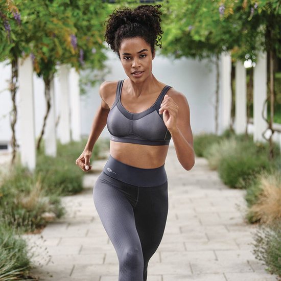 Model rent in een antracietkleurige sportbeha en legging, met ademende mesh stof.
