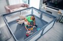 Grijze babybox met speelgoed, een moeder en baby binnen. De box heeft een kattenmotief op de panelen.
