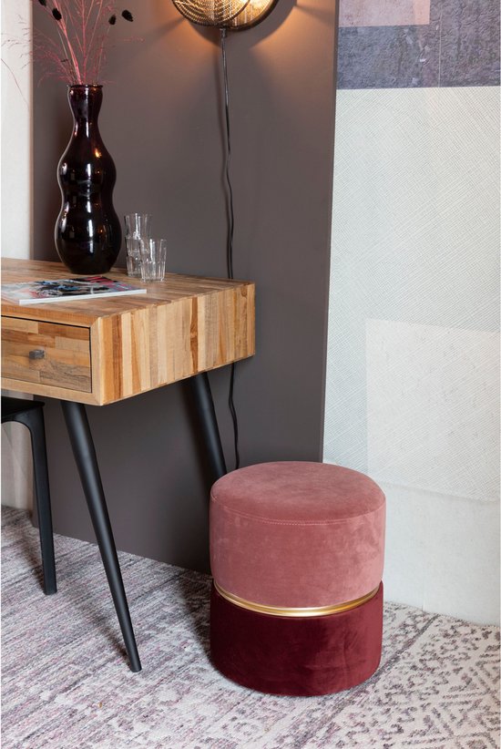 Ronde poef met een lichtroze bovenkant en een donkerrode onderkant, gescheiden door een gouden ring. Staat naast een bureau.