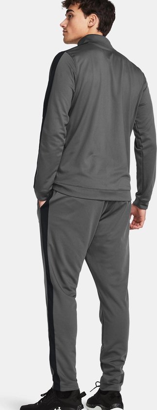 Achterkant van een man in grijs Under Armour trainingspak met zwarte streep op het been en de mouw.