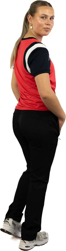 Model draagt een rode sporttop met donkerblauwe mouwen, zwarte trainingsbroek en witte sportschoenen.