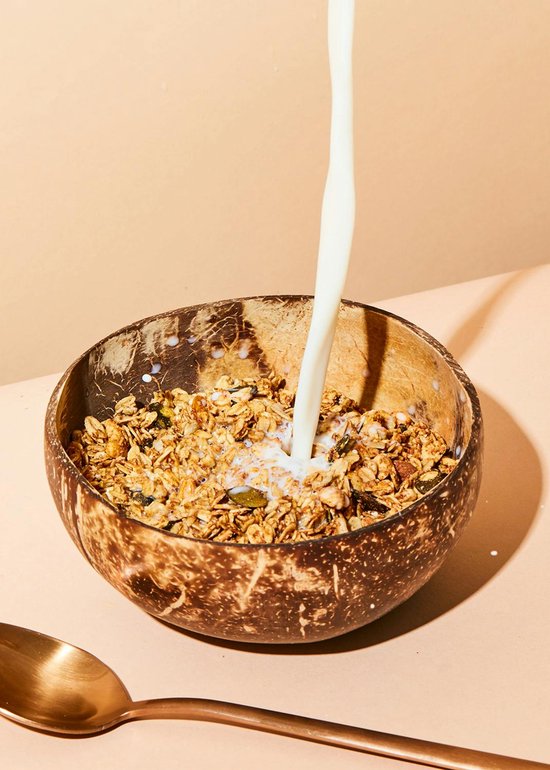 Kokosnootschaal gevuld met knapperige biologische granola en noten, met melk die erin wordt gegoten.