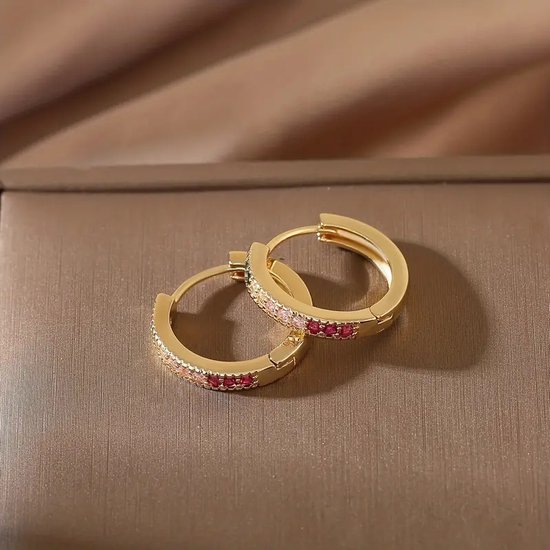 Gouden oorringen bezet met roze en rode zirkonen, glanzend.