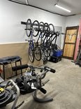 Een garage met een zwart fietsophangsysteem aan de muur waarop vijf fietsen hangen.