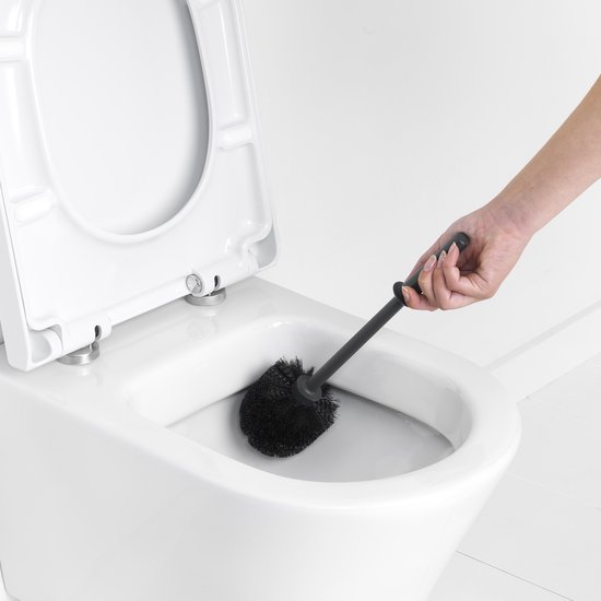 Main utilisant un balai WC noir dans une cuvette de toilette.