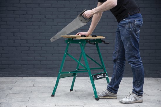 Een man in spijkerbroek zaagt met een handzaag op een groene, opvouwbare werkbank met bamboe werkblad.