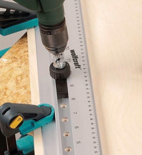 Close-up van een wolfcraft deuvelmal met boor die een gat boort in een houten plank.
