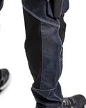 Detail van de onderkant van een werkjeans, met donkerblauwe denim en zwart verstevigd materiaal.
