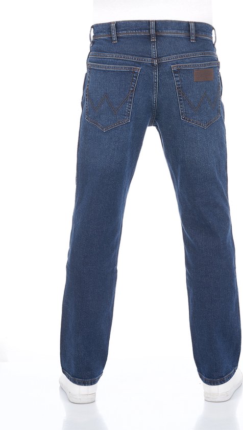 Achterkant van een man in een loszittende, blauwe Wrangler jeans met witte sneakers.
